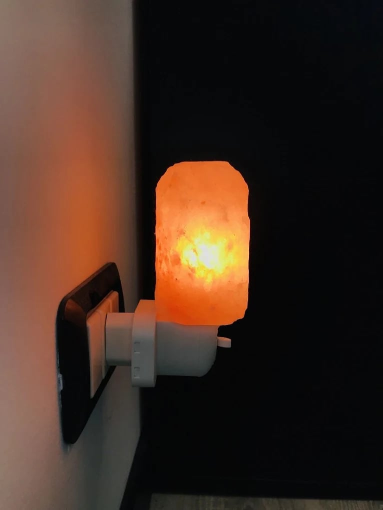 Himalayan salt lamp plugged into wall outlet glowing warm orange and yellow light against dark background