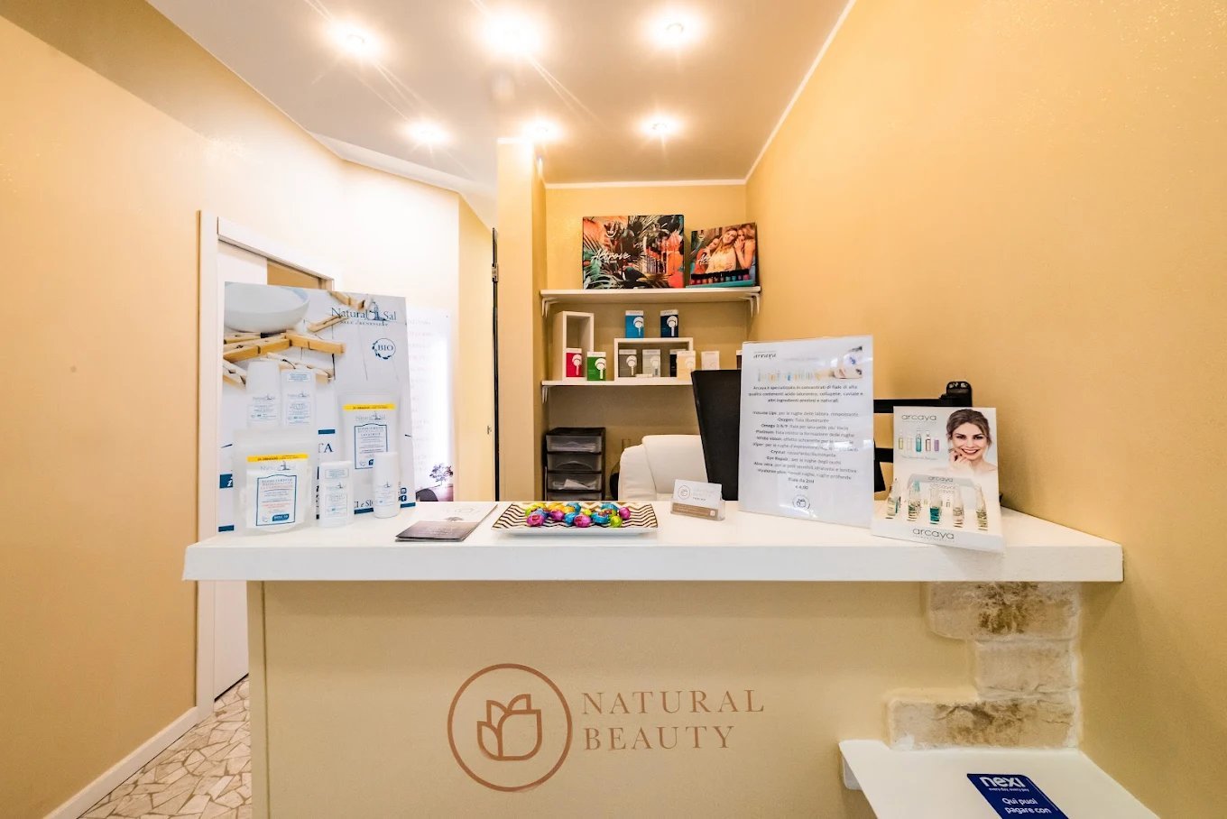 Modern beauty salon reception desk with natural beauty branding, product displays, and warm lighting in a welcoming yellow-toned space
